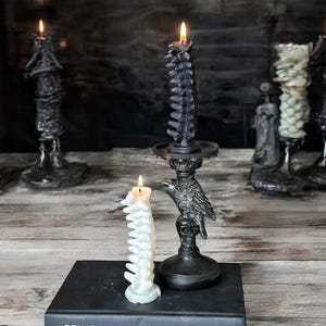 Pode incluir: Duas velas em forma de espinha dorsal, uma preta e outra branca, em casti&ccedil;ais pretos. A vela preta est&aacute; em um casti&ccedil;al em forma de corvo. As velas est&atilde;o em um livro intitulado "Prince Harry Spare".