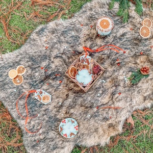 May include: A white faux fur rug with a variety of decorative items, including candles, dried orange slices, and cinnamon sticks. The items are arranged in a rustic and cozy style.