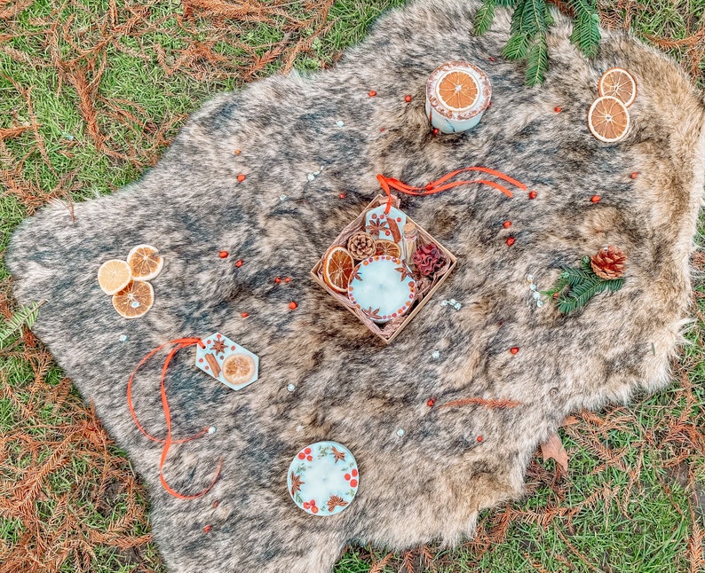 May include: A white faux fur rug with a variety of decorative items, including candles, dried orange slices, and cinnamon sticks. The items are arranged in a rustic and cozy style.