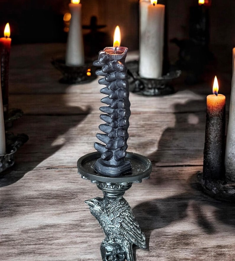 Pode incluir: Uma vela preta em forma de espinha dorsal est&aacute; sobre um casti&ccedil;al em forma de corvo. A vela est&aacute; acesa e o casti&ccedil;al &eacute; de metal.
