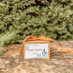 May include: A brown box with a tan ribbon tied around it. The box has a label that says "Handmade Monlix Candles London".