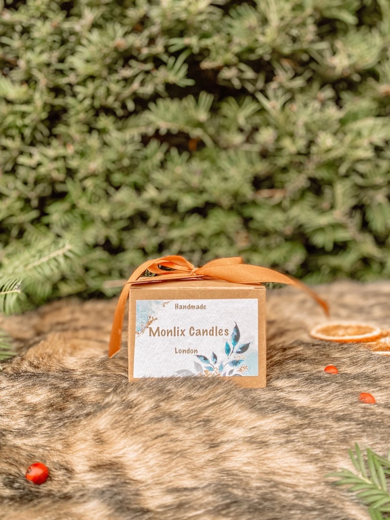 May include: A brown box with a tan ribbon tied around it. The box has a label that says "Handmade Monlix Candles London".