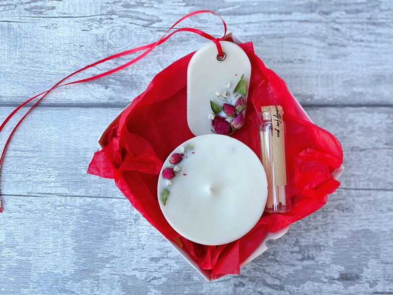 May include: A white gift box with red tissue paper. The box contains a white candle with dried flowers, a white wax melt with dried flowers, and a small glass vial with matches. The vial has a label that says "specially for you".