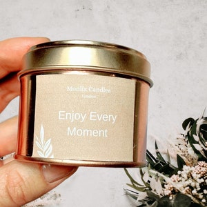 May include: A gold tin candle with a beige label that reads "Monlix Candles London" and "Enjoy Every Moment".