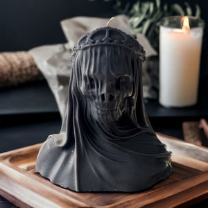 May include: Black candle in the shape of a hooded figure wearing a crown. The candle is sitting on a wooden tray.
