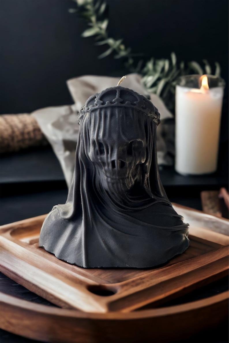 May include: A black candle in the shape of a hooded figure wearing a crown. The candle is sitting on a wooden tray.