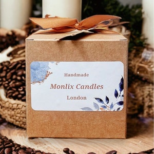 Pu&ograve; includere: Una scatola di cartone marrone con un nastro marrone legato intorno. La scatola ha un'etichetta bianca con disegni ad acquerello blu e oro e il testo "Handmade Monlix Candles London".