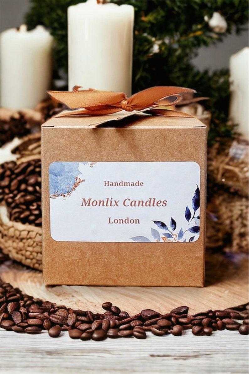 Pu&ograve; includere: Una scatola di cartone marrone con un nastro marrone legato intorno. La scatola ha un'etichetta bianca con disegni ad acquerello blu e oro e il testo "Handmade Monlix Candles London".
