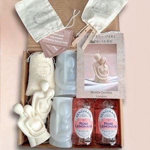 May include: A gift box filled with a couple's candle making kit. The kit includes two clear silicone molds, two white couple's candles, two small white muslin bags, two bottles of rose lemonade, and a card with the text "One of the fondest memories with you. What."