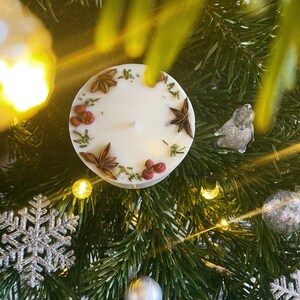 May include: A white candle with a decorative ring of dried herbs and spices. The candle is on a green Christmas tree.
