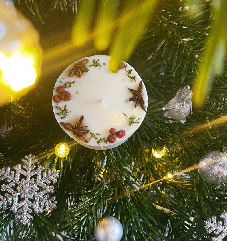 May include: A white candle with a decorative ring of dried herbs and spices. The candle is on a green Christmas tree.