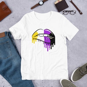 May include: White t-shirt featuring a graphic of a dripping, multi-coloured lip print. The lip is divided into four sections: yellow, white, purple, and black.