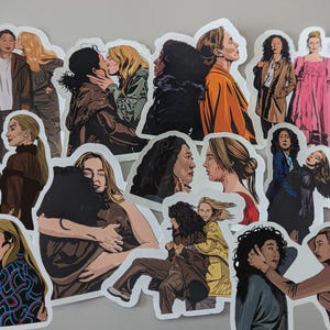 May include: A selection of die-cut stickers showcasing illustrations of two women in different poses. The stickers portray scenes of closeness, hugs, and interaction, with an emphasis on the characters' expressions and attire. The colour scheme includes browns, oranges, and blues.
