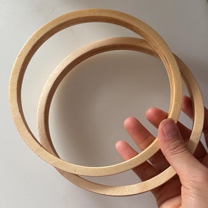 Puede incluir: Dos aros de bordado de madera, uno dentro del otro, con un acabado de madera natural.