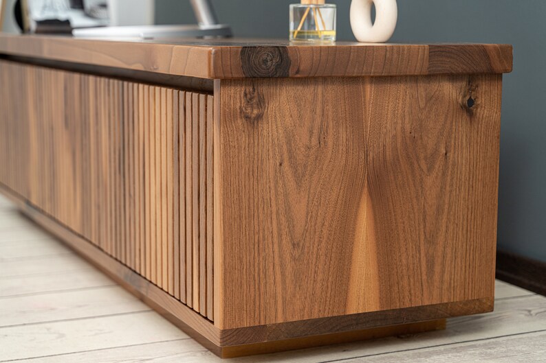 Op de afbeelding: Een houten entertainmentcenter met een lamellendeurontwerp. De kast is gemaakt van donkerbruin hout met een natuurlijke houtnerf.