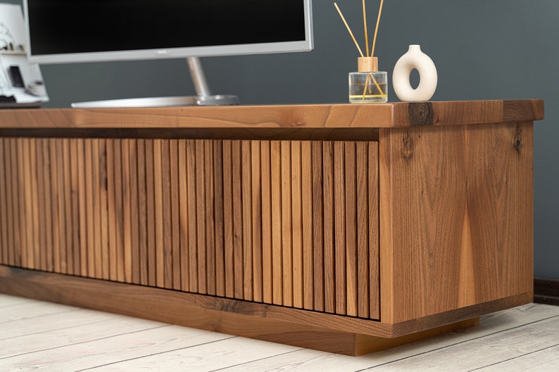 Op de afbeelding: Een houten tv-meubel met een lamellenfront en een donkerbruine afwerking. Het meubel heeft een eenvoudig, modern ontwerp en is perfect voor het presenteren van een televisie of andere media-apparatuur.