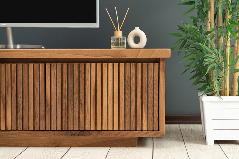 Op de afbeelding: Een houten tv-meubel met een lamellenfront, afgewerkt in donkerbruin. Het meubel heeft een eenvoudig ontwerp en is perfect voor het presenteren van een televisie en andere media-apparatuur.