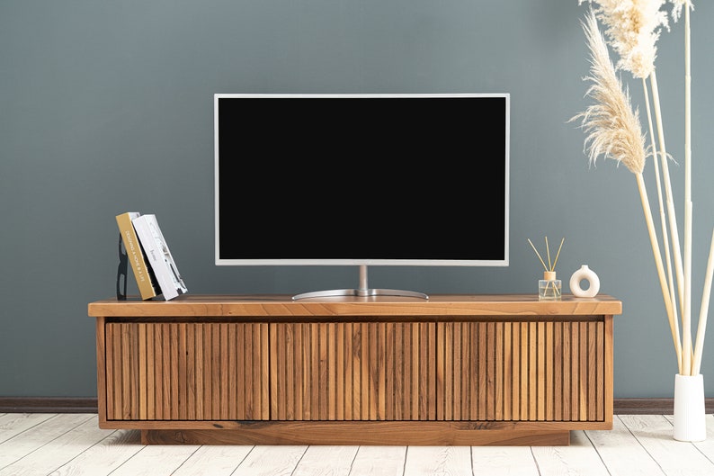 Op de afbeelding: Een houten tv-meubel met drie lamellen deuren. Het meubel is gemaakt van lichtbruin hout en heeft een modern ontwerp. Een flatscreen tv staat op het meubel.