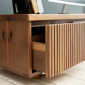 Op de afbeelding: Een houten entertainmentcenter met een lade en twee deuren. De deuren hebben verticale latten en staan open, waardoor de binnenkant van de kast zichtbaar is. De kast is gemaakt van donker hout met een natuurlijke afwerking.