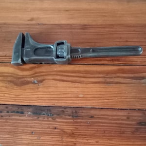 Puede incluir: Una llave inglesa negra con un pomo de ajuste plateado. La llave está sobre una superficie de madera.
