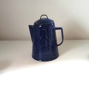 Puede incluir: Una cafetera de esmalte azul con motas blancas. La cafetera tiene un asa y un pico.