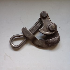 May include: A robust metal wire grip tool, featuring a loop and a hinged clamp. The tool has a dark, aged grey hue, with the text "NA STONE CHICAGO" visible. It's designed for gripping and pulling wires or cables, a practical tool.