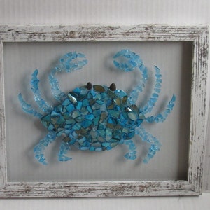 May include: A blue glass mosaic crab framed in white distressed wood. The crab is made of many small pieces of blue glass.