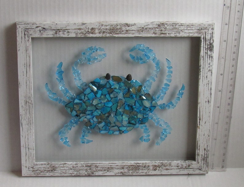 May include: A blue glass mosaic crab framed in white distressed wood. The crab is made of many small pieces of blue glass.