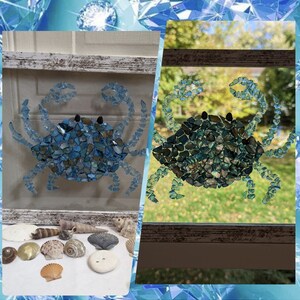 May include: A blue crab mosaic made from small pieces of iridescent glass. The crab is displayed in a white frame with a rustic wood finish.