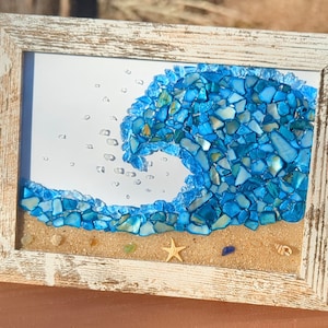 May include: A framed artwork depicting a blue wave made of glass mosaic tiles. The wave is crashing over a sandy beach with a starfish and seashells.
