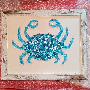 May include: A blue crab mosaic made from broken pieces of glass, framed in a white distressed wood frame.