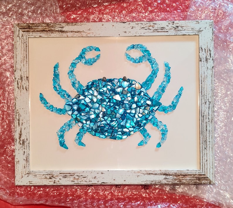 May include: A blue crab mosaic made from broken pieces of glass, framed in a white distressed wood frame.