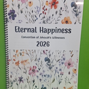 May include: A spiral-bound notebook featuring a watercolor floral pattern with various wildflowers in shades of pink, orange, purple, and blue. The cover displays the text Eternal Happiness, Convention of Jehovah's Witnesses, and the year 2026.