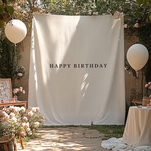 May include: A birthday party scene with a white backdrop that reads "HAPPY BIRTHDAY". Two large white balloons are suspended in the air. The scene is decorated with flowers and a table with a cake.