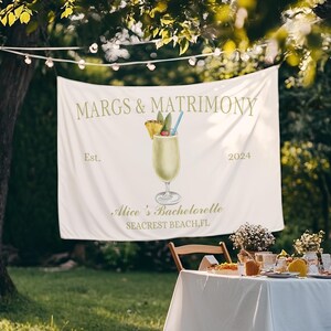 Op de afbeelding: Witte banner met de tekst "MARGS & MATRIMONY Est. 2024" en een tekening van een ananas-margarita. Onder de tekening staat de tekst "Alice's Bachelorette SEACREST BEACH, FL"