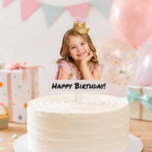 Può includere: Un topper per torta in acrilico trasparente con una stampa fotografica di un bambino sorridente che indossa una corona glitterata dorata. Il topper ha una forma sagomata e il testo nero "HAPPY BIRTHDAY!" su una torta bianca.