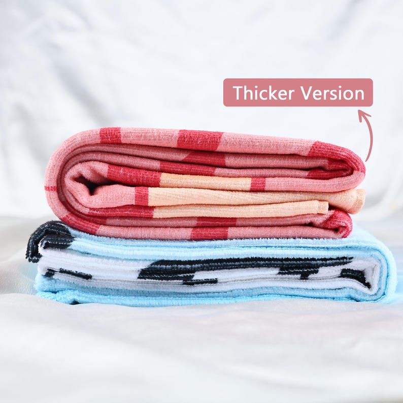 May include: Folded towels in shades of pink, red, and blue. The top towel has a pink and red checkered pattern. The bottom towel is light blue with a black and white pattern. The text "Thicker Version" is in the image.