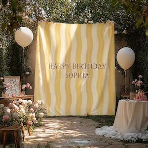 Puede incluir: Un gran telón de fondo rectangular de tela con rayas verticales onduladas en tonos alternos de crema y amarillo. El texto HAPPY BIRTHDAY SOPHIA está impreso en una fuente serif marrón oscuro centrada en el panel de tela.