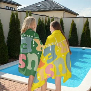 May include: Two beach towels with colorful designs. One is green with a retro-style design and the word "Harris" in white script. The other is yellow with a similar design and the word "Harris" in white script. Both towels are near a swimming pool.