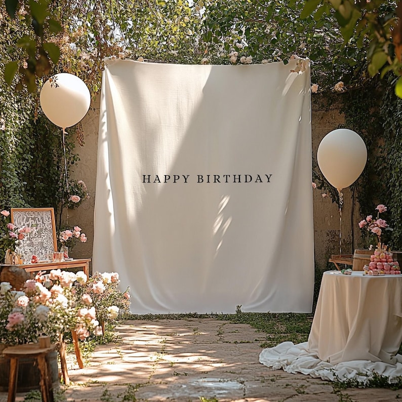 Puede incluir: Escena de fiesta de cumplea&ntilde;os con un tel&oacute;n de fondo blanco que dice "HAPPY BIRTHDAY". Se ven dos grandes globos blancos. La escena est&aacute; decorada con flores y una mesa con una tarta.