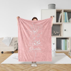Peut inclure: Une couverture en polaire rose avec un motif floral blanc et le nom "Damla" imprim&eacute; dessus.