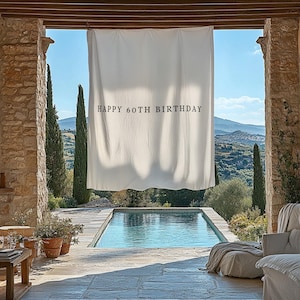 Puede incluir: Una pancarta de tela blanca con el texto "HAPPY 60TH BIRTHDAY" cuelga frente a una piscina. La escena est&aacute; enmarcada por columnas de piedra y una vista de una cordillera y cielo azul.