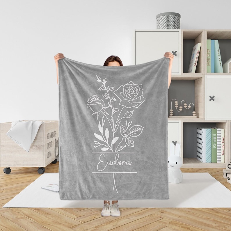 Peut inclure: Jet&eacute; de canap&eacute; en polaire gris avec un contour blanc d'un bouquet de roses et le nom "Eudora" imprim&eacute; dessus.