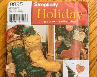 May include: A Simplicity Holiday pattern collection featuring Christmas stocking designs. The cover displays images of green, gold, and red stockings with decorative elements. Additional ornaments and a tree skirt are also shown. The pattern is one size.