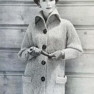 Puede incluir: Un cárdigan de punto de color claro con botones grandes y bolsillos. El cárdigan tiene un cuello ancho. La textura de punto es visible y el estilo general es clásico. La persona lleva el cárdigan.