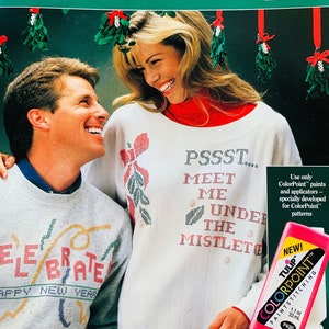 May include: A couple wearing white sweaters with colorful holiday-themed designs. The woman is holding a bottle of pink paint labeled "ColorPoint" and "TULIP". The text on the sweaters reads "Celebrate Happy New Year" and "PSSST... Meet Me Under The Mistletoe".