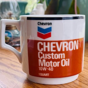 May include: White ceramic mug with a red, white, and blue Chevron logo and the text "Chevron Custom Motor Oil 10W-40 1 Quart".