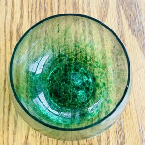 Puede incluir: Un cuenco redondo de vidrio con un dise&ntilde;o moteado verde y amarillo. El cuenco tiene un borde verde oscuro y un interior claro y reflectante. El cuenco est&aacute; sobre una superficie de madera.