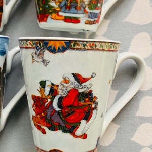 May include: White ceramic mug with a Christmas scene featuring Santa Claus riding a reindeer. The mug has a blue and gold trim around the top.