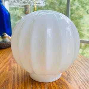 May include: A spherical white milk glass light globe featuring a vertical ribbed texture. The lamp shade has a smooth, rounded top and a circular opening at the base for attachment to a fixture, presenting a clean and opaque appearance.